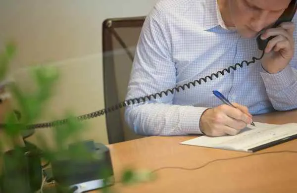 Man on a phone writing on a legal pad.